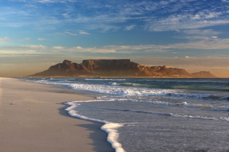 Sandy beach with ocean waves and Table Mountain in the distance on luxury Cape Town trips.