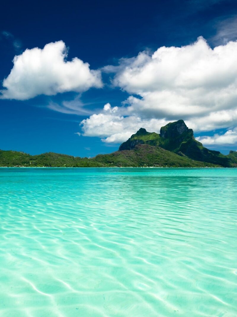 Lush green mountain peak overlooking a turquoise tropical lagoon on luxury French Polynesia tours.