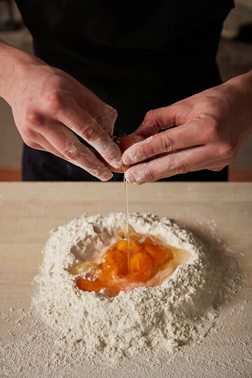 Hands cracking an egg into a pile of flour and yolks on a wooden surface. luxury food and wine holidays.