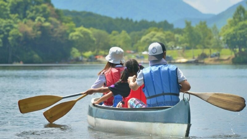 People rowing a blue canoe on a calm lake with mountains in the distance during luxury Family vacations.