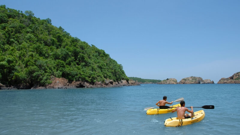 Two people paddle yellow kayaks through a calm coastal bay on luxury Latin America family tours.