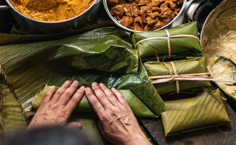 Hands wrapping food in banana leaves for luxury Southeast Asia trips.