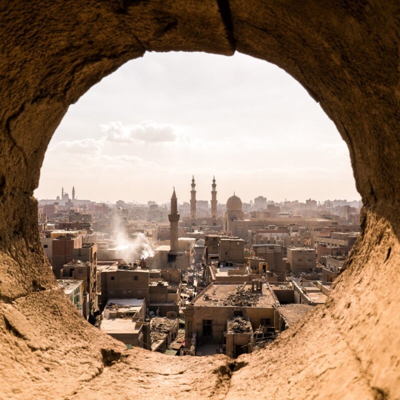 Luxury Egypt Tours - view of a desert city with a mosque through a round viewpoint in a wall