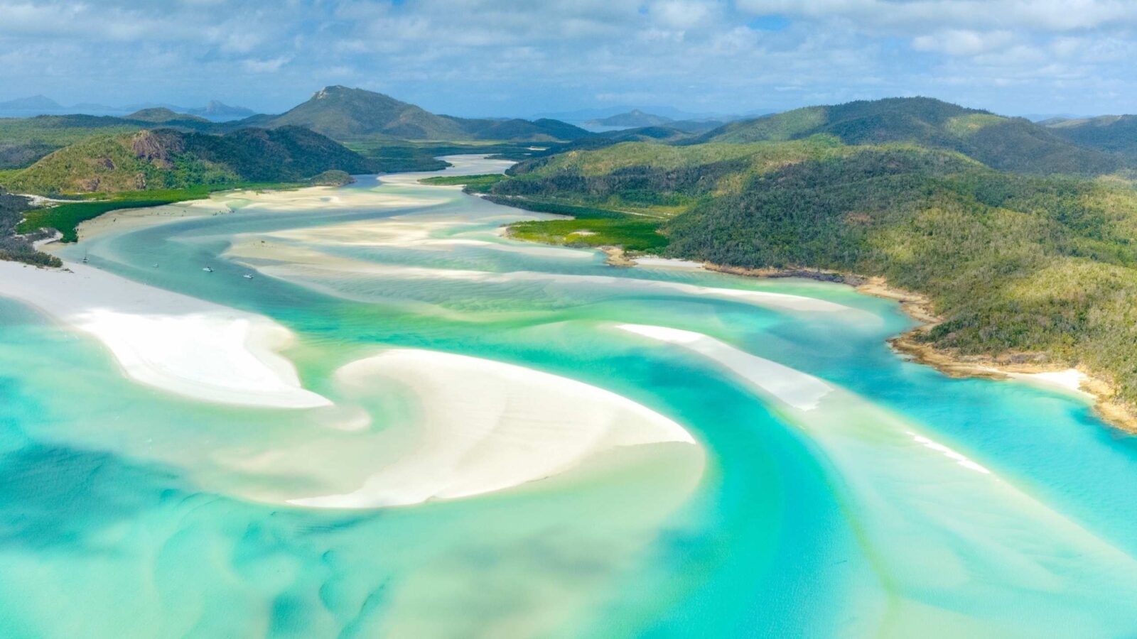 Aerial view of white sand bars swirling through turquoise tropical ocean water surrounded by green hills.