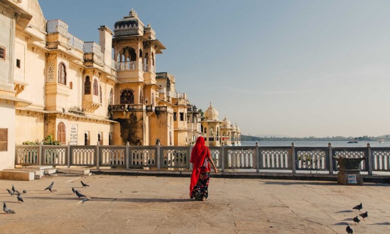 A woman in a red sari walking towards the railings of a viewpoint over a river