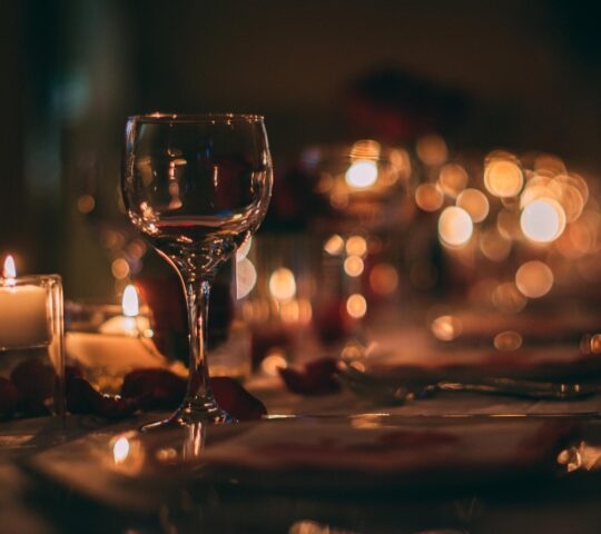 Elegant dinner setting with a wine glass, candles, and warm bokeh lights.