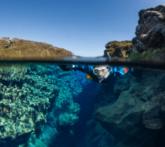 Over-under shot of a crystal clear lake with underwater rocks and a diver.