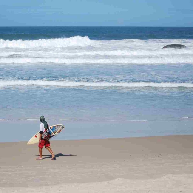A surfer walks along the beach in Florianópolis