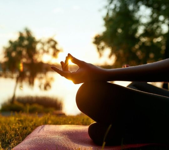 Close up image of a woman practising yoga outdoors, with trees and a lake in the background