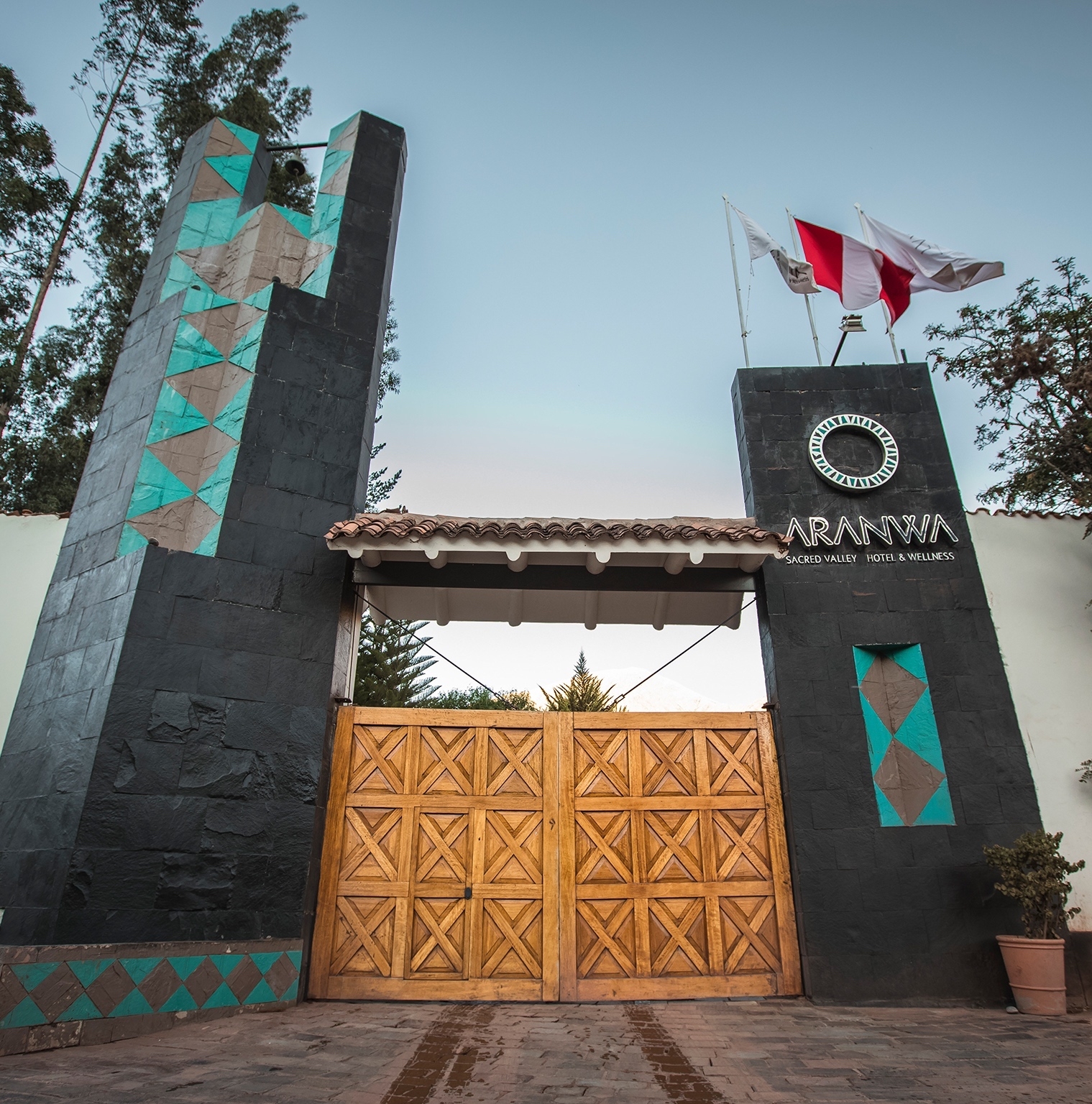 Entrance gate to Aranwa Sacred Valley Hotel & Wellness with flags above and geometric designs on pillars.