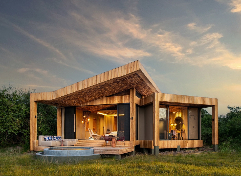 Modern wooden safari lodge with a private plunge pool on a deck, set against a lush green landscape at sunset.