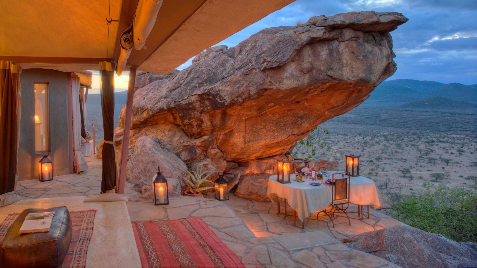 A candlelit dinner table set on a rocky terrace under a giant boulder at Saruni Samburu honeymoon villa.
