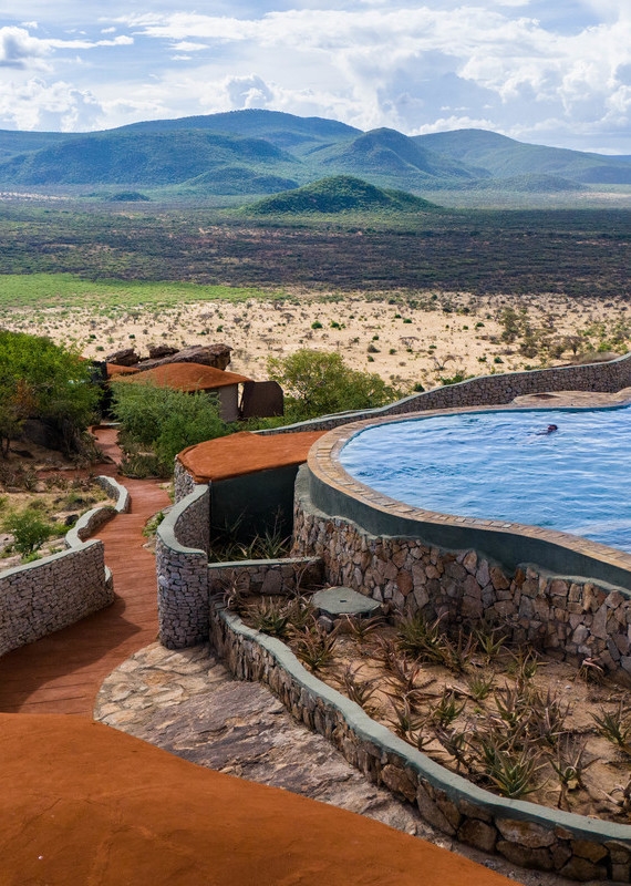 A swimming pool on a rocky cliff with a stone path leading toward distant blue mountains at Saruni Samburu.