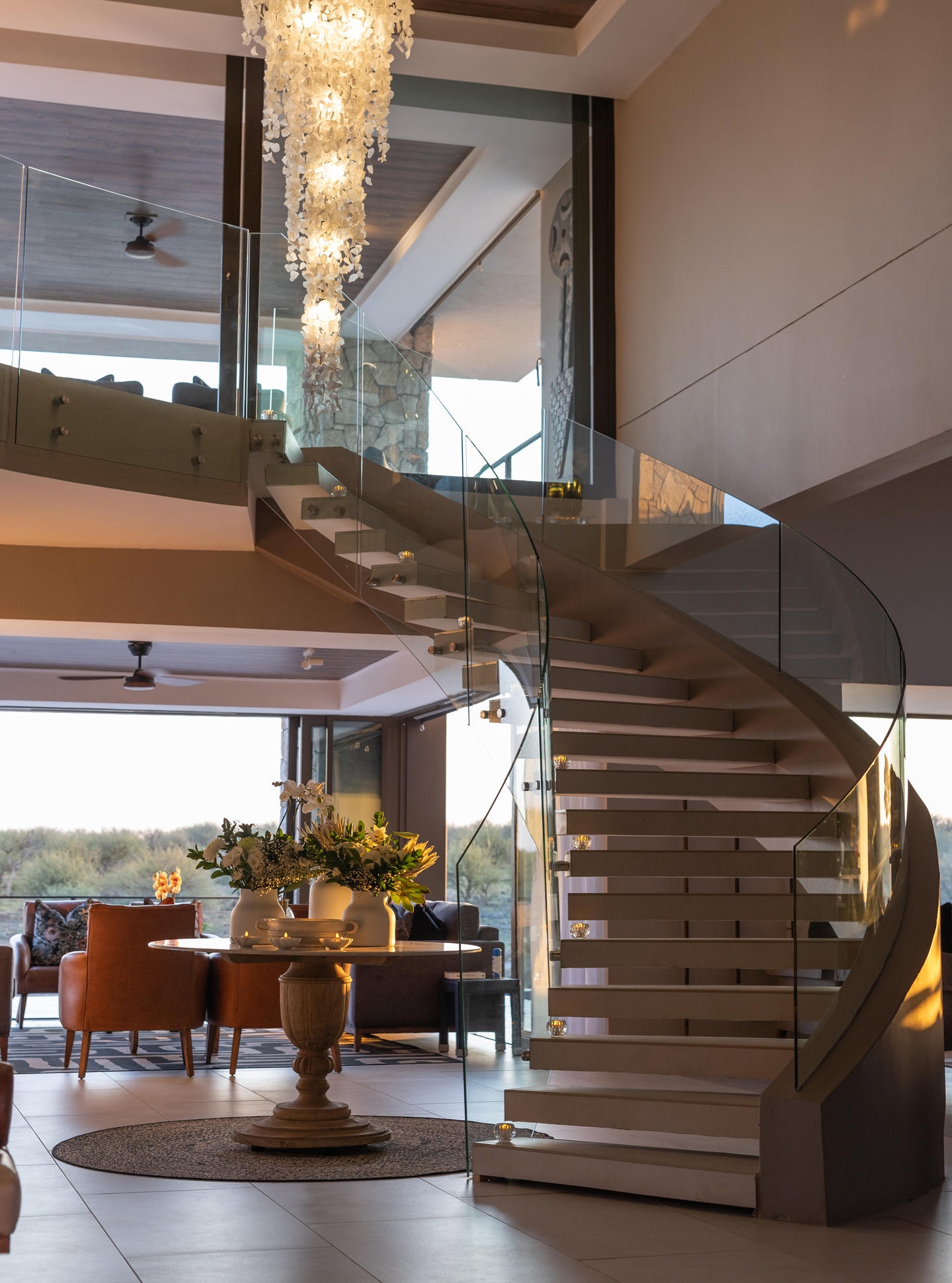 Modern interior with spiral staircase, glass balustrade, and elegant chandelier.