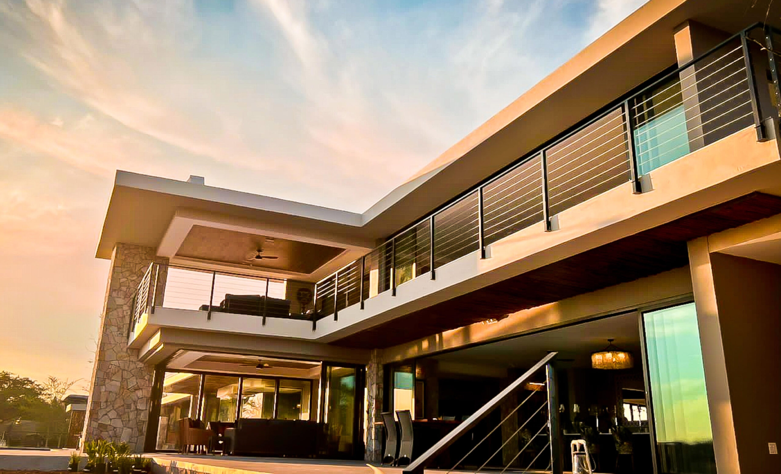 Modern two-story house with glass balconies at sunset.