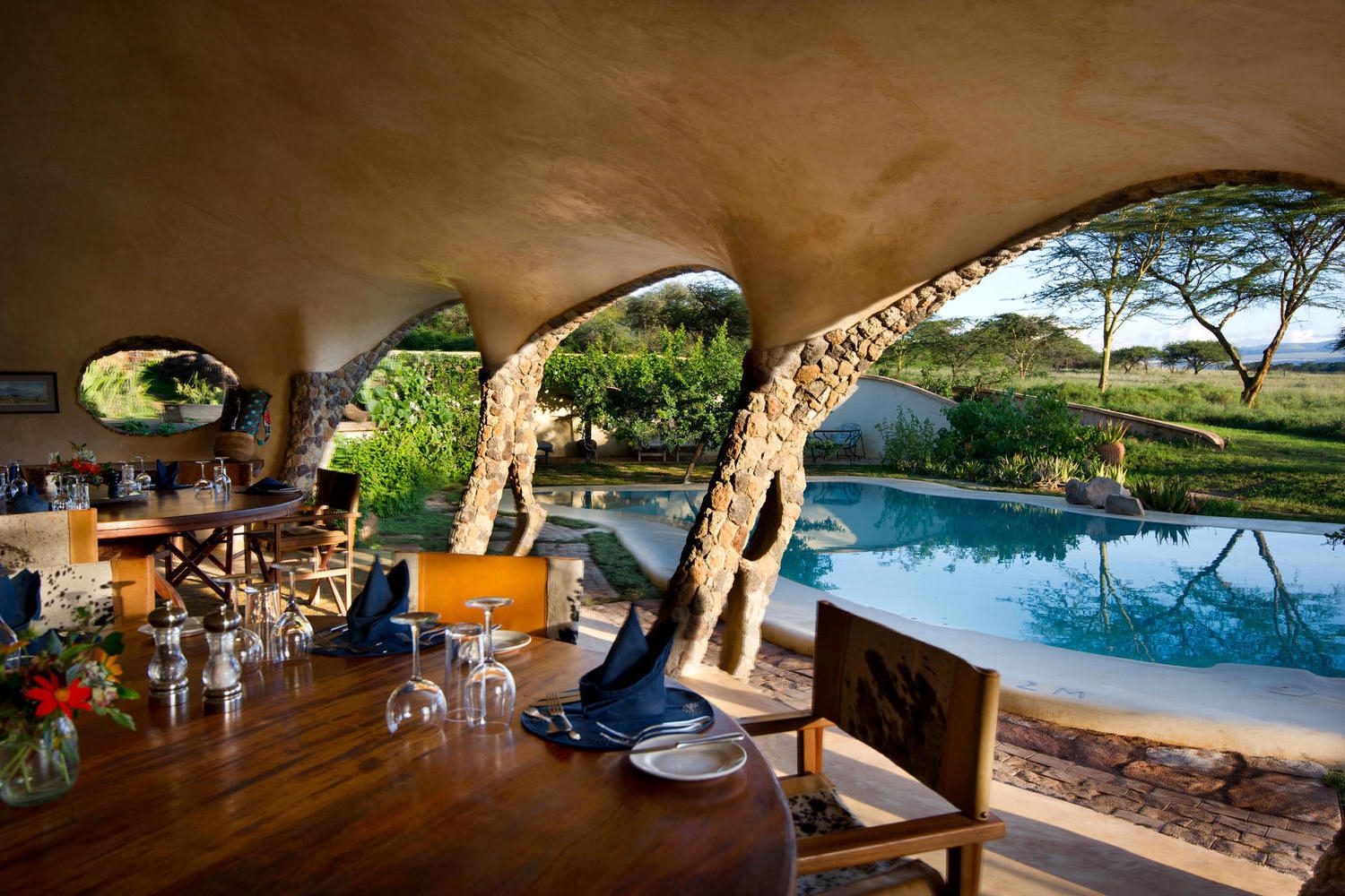 Interior view of a dining room with stone pillars and a view of a pool and the savanna.
