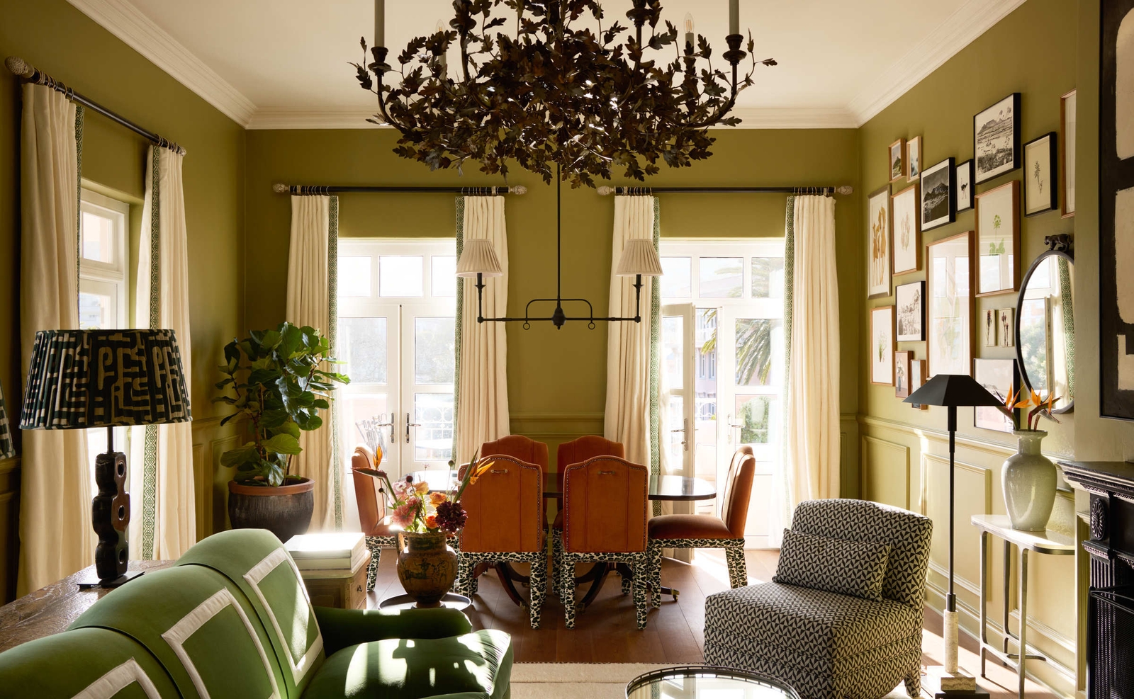 Elegantly decorated lounge with olive walls, a large dark chandelier, patterned furniture, and many framed pictures.