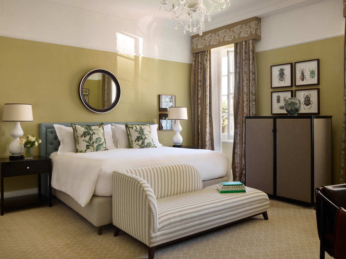 Elegant hotel room at Mount Nelson Cape Town with a large bed, botanical pillows, and a striped settee.