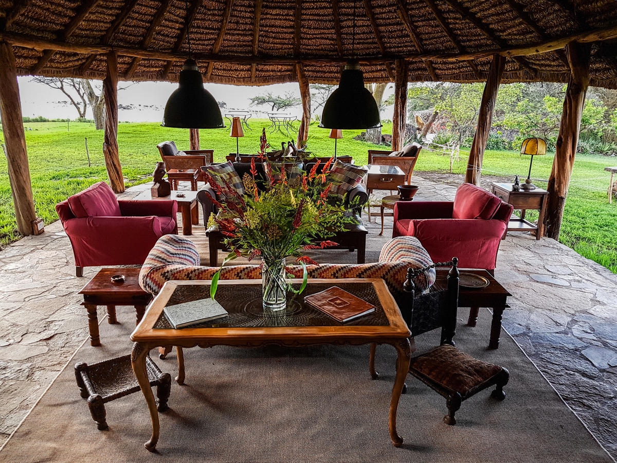 An open-air lounge with red chairs and a thatched ceiling overlooking a green landscape.