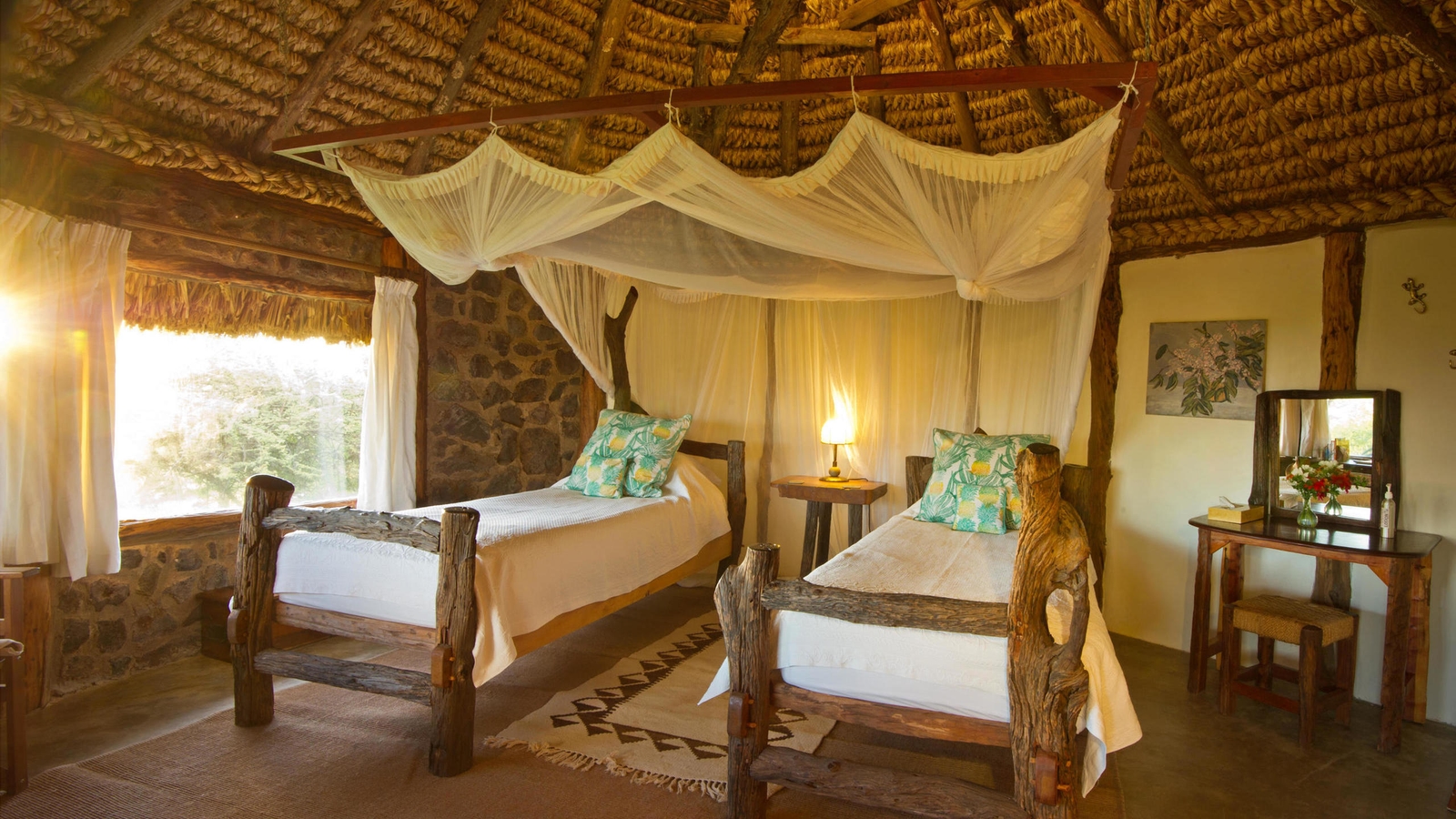 Two twin beds with white linens and mosquito nets in a rustic room with stone walls.
