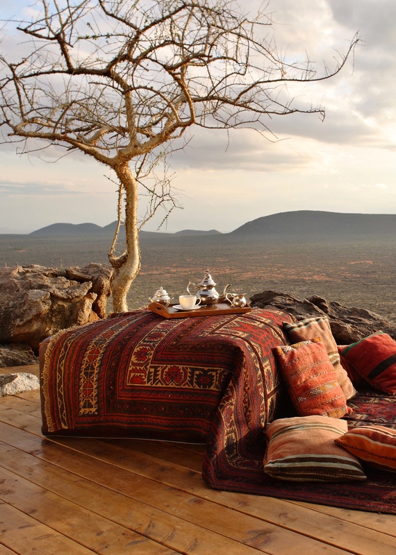 A tea tray on a patterned ottoman with cushions on a wooden verandah overlooking a valley at Saruni Samburu.