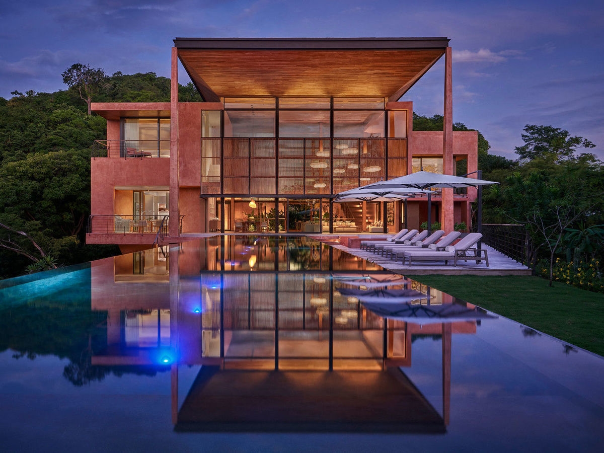 Modern two-story villa with a large infinity pool reflecting the building and purple dusk sky.