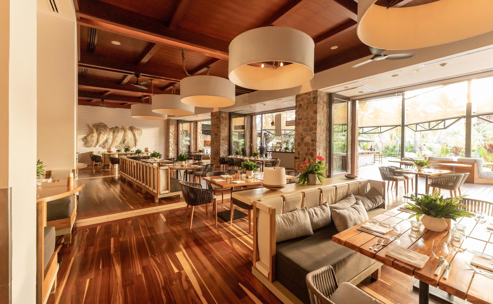 Large modern dining room with wooden floors, neutral furniture, and oversized white hanging lamps.