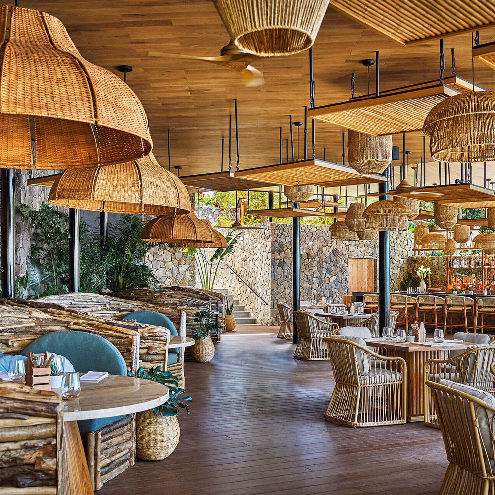 Elegant restaurant interior with large woven pendant lamps, wooden tables, and stone walls.