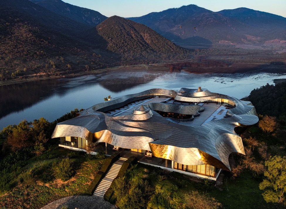 Aerial view of Vik Chile showing a modern building with a flowing silver metal roof overlooking a lake and mountains.