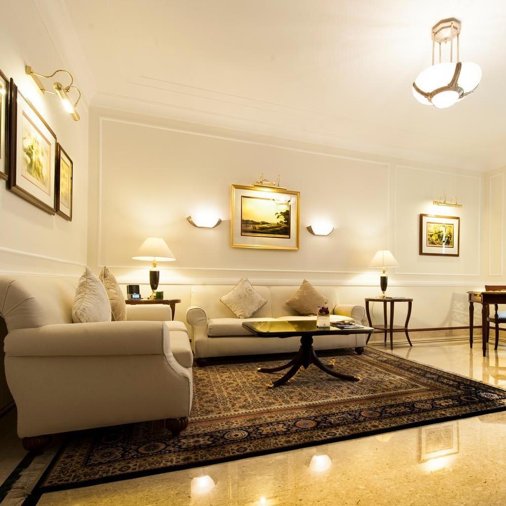An elegant living room with white sofas, a large ornate rug, and warm wall lighting in a Heritage Suite.