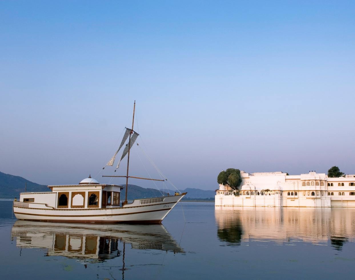 A sailing boat on a lake in the foreground with the Taj Lake Palace in the background.