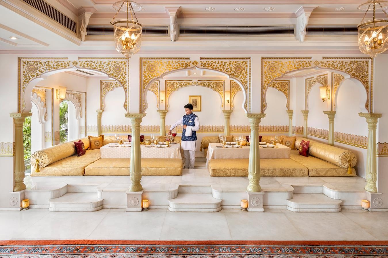A person pouring a beverage in a cushioned dining area at the Taj Lake Palace.