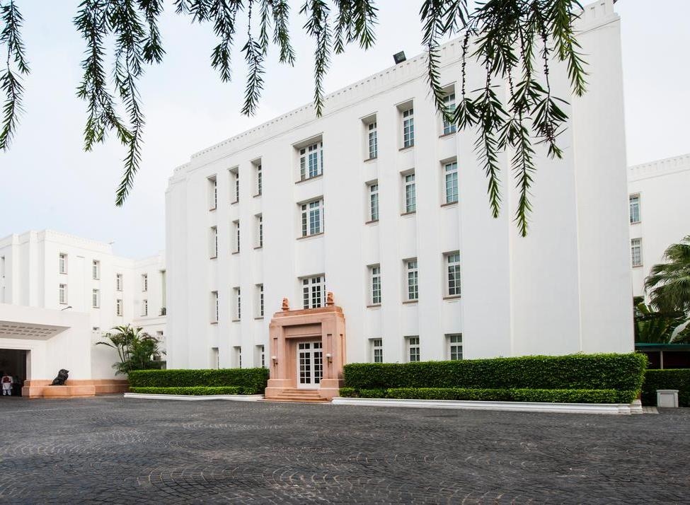 The white exterior of The Imperial Delhi India with a tan stone doorway and manicured green bushes along the base.