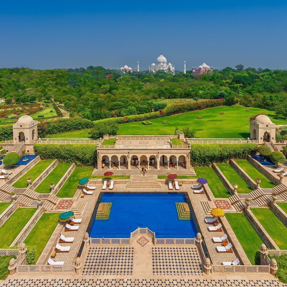 Symmetrical swimming pool at The Oberoi Amarvilas surrounded by green lawns, stone terraces, and white lounge chairs.