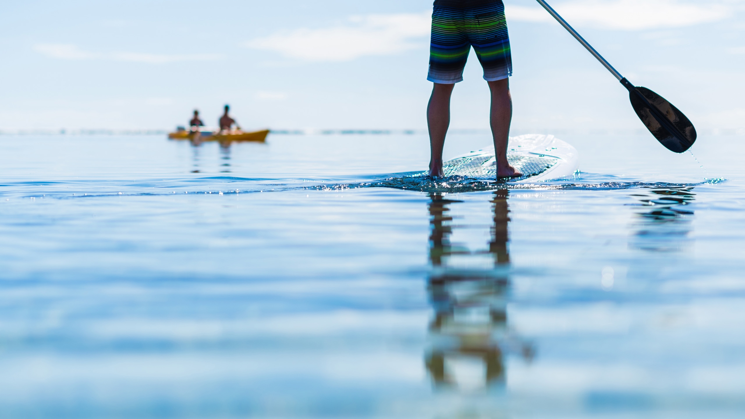 Close up of a person's legs as they stand on a paddle board in calm water