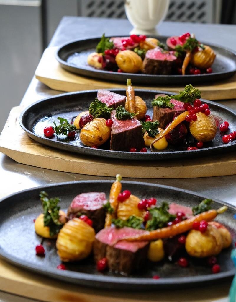 Close-up of three black plates containing steak, potatoes, and berries, ready for serving.
