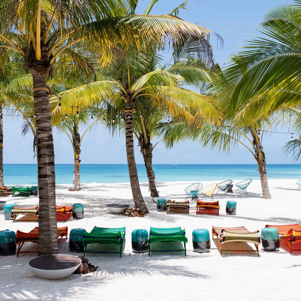 Vibrant green and orange beach loungers under palm trees on a white sand beach at Zuri Zanzibar.
