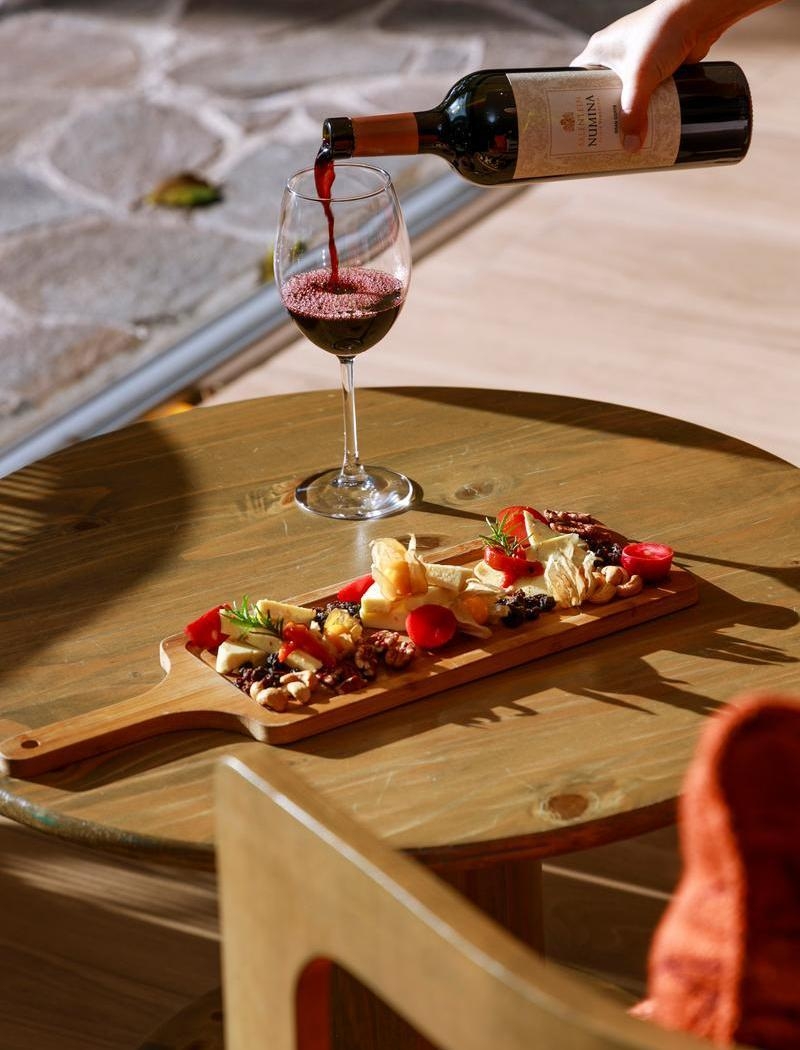 A close-up of a cheese board and red wine being poured into a glass.