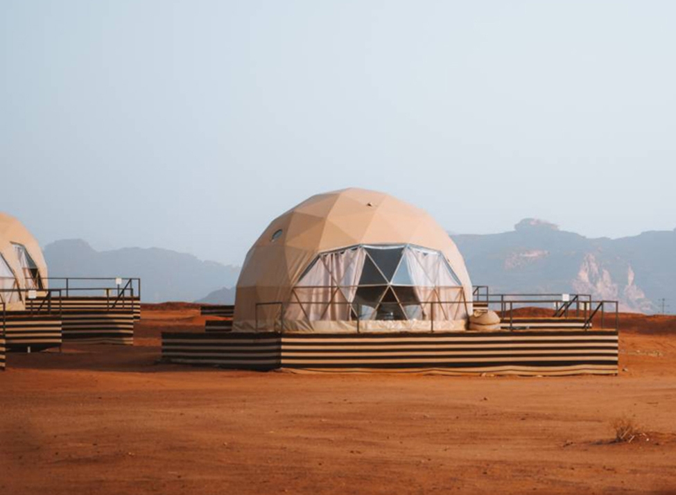 A geodesic dome tent at Sun City Camp in Wadi Rum, Jordan, nestled against jagged desert rock formations under bright sun.