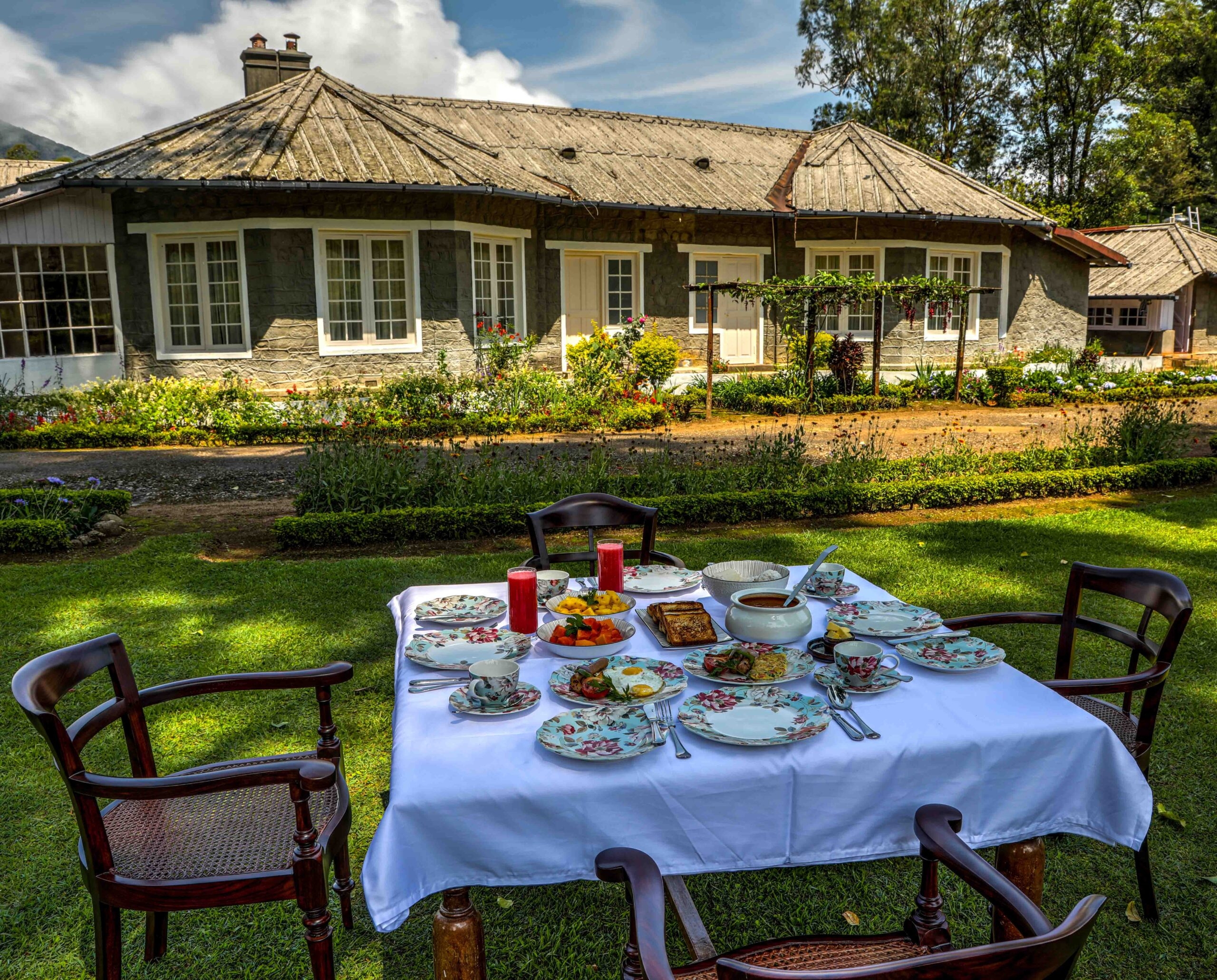 Outdoor dining setup with food on table in garden by a cottage.