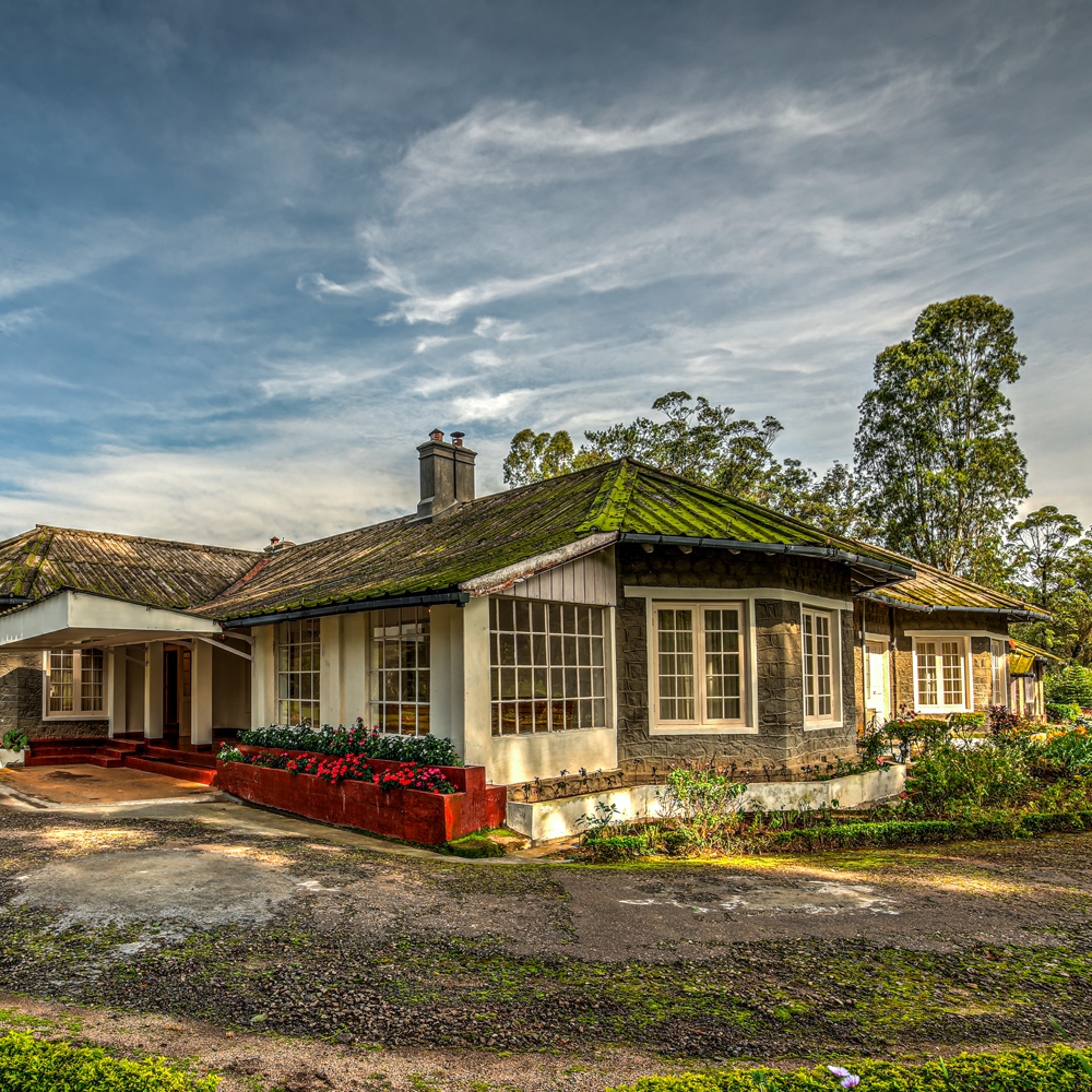 Old cottage with mossy roof against a blue sky, surrounded by greenery.