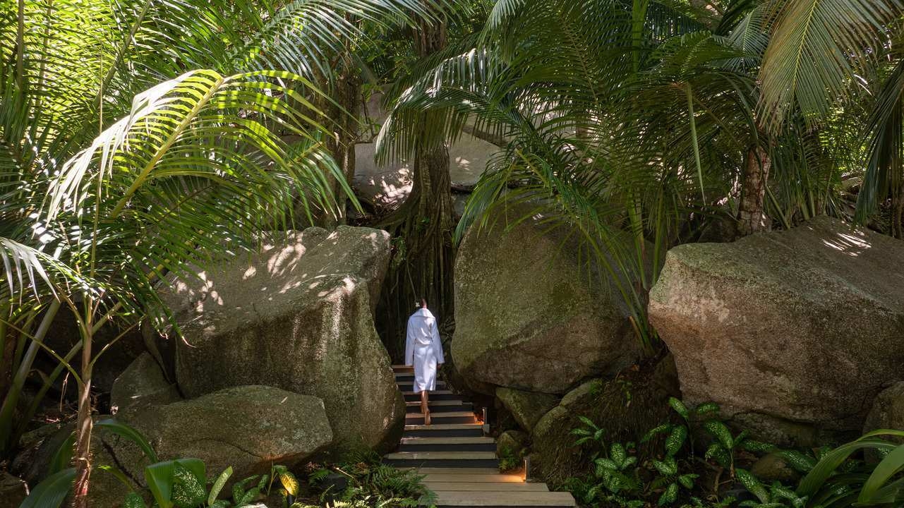 A woman walking into the spa area of Cheval Blanc Seychelles, that blends into its surroundings of granite boulders and palms.
