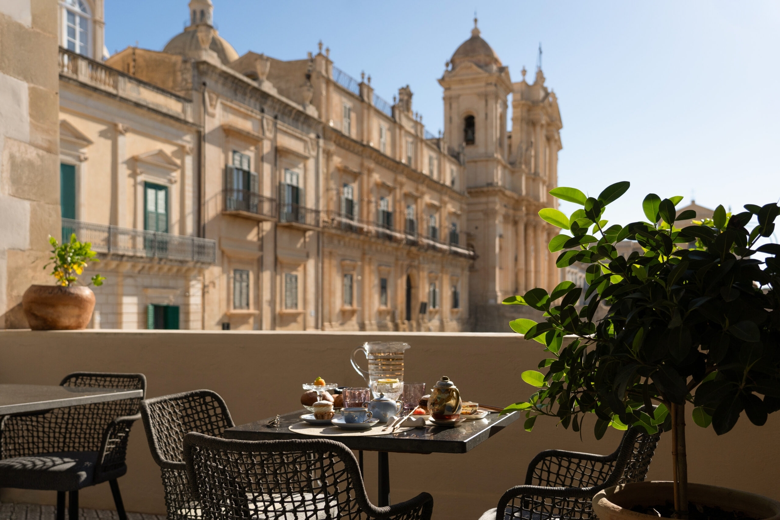 Outdoor terrace with tables and chairs with blue cushions overlooking the tops of several historic buildings in the background.