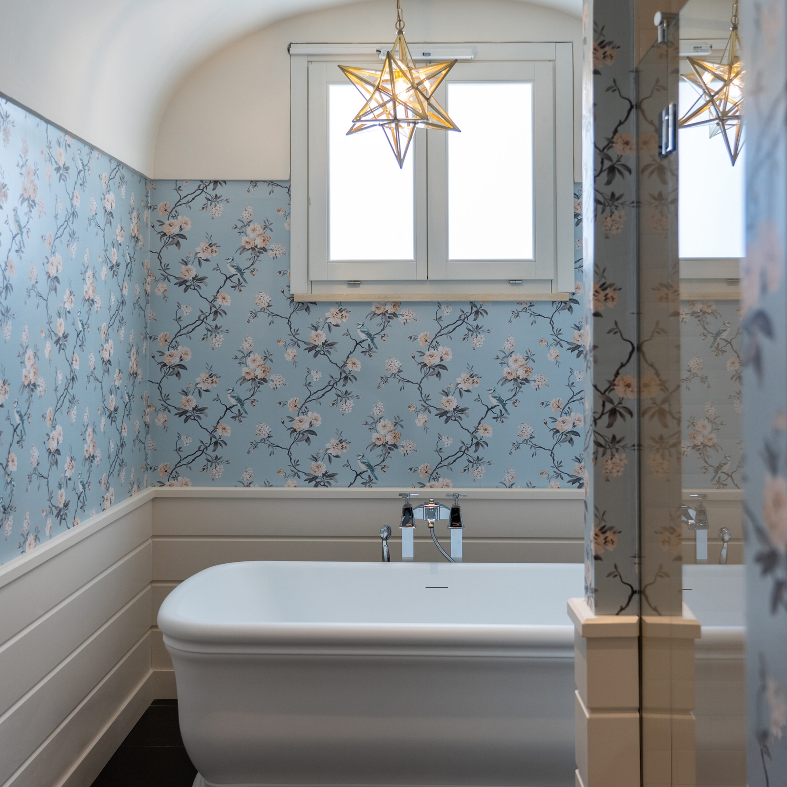 Interior of a bathroom with a freestanding bathtube and blue floral wallpaper on the walls.