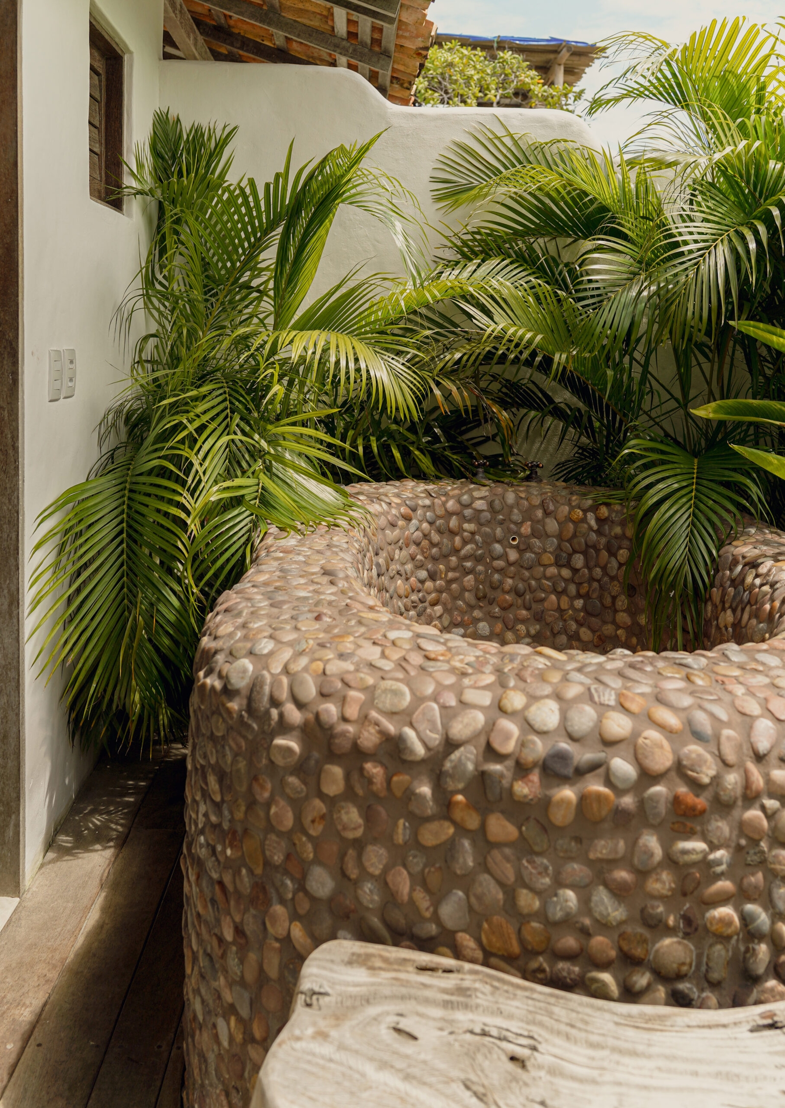 Exterior of a round soaking tub made of concrete and stones, surrounded by green ferns.