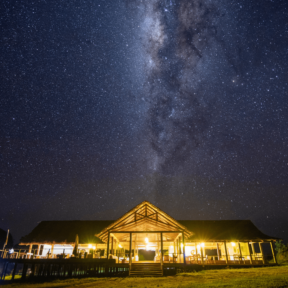 Mboko Lodge's wooden pavilion illuminated at night, with a starry sky above