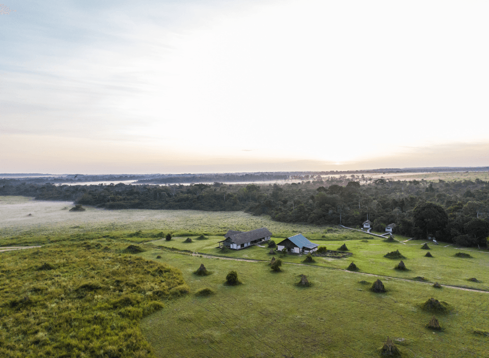 Wide view of Mboko Lodge, set on a wide grassy plain next to a river and forest