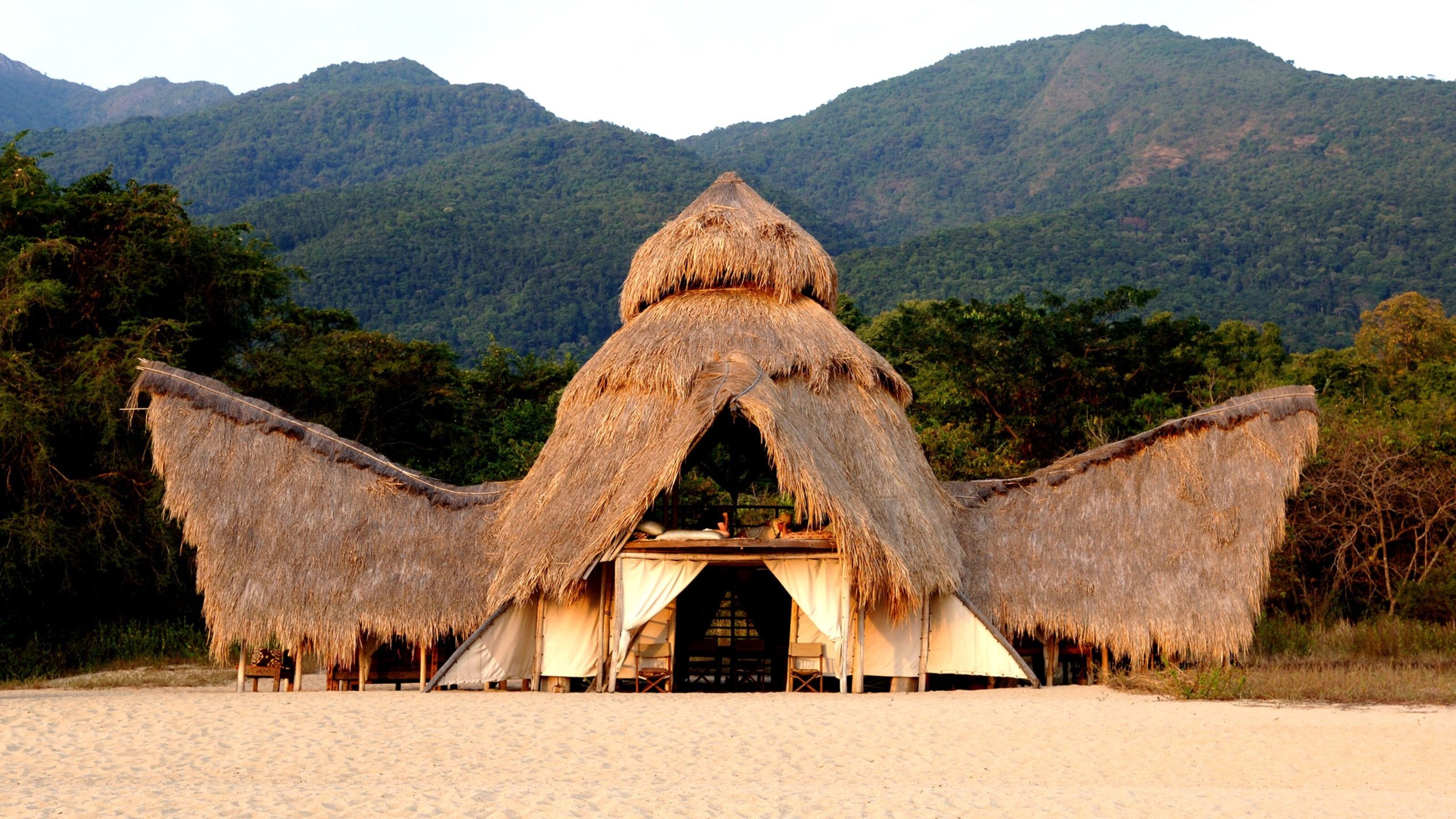 Exterior of Greystoke Mahale constructed of recycled dhows and thatched palm leaf roof set in front of the Mahale Mountains, Tanzania