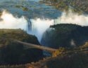 Aerial view of a stunning waterfall surrounded by lush greenery, with a bridge crossing over a gorge below the misty falls.