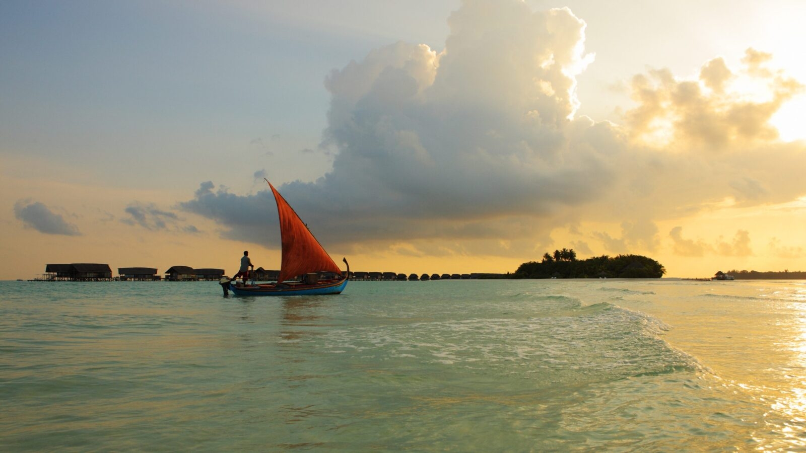 A red sailed boat on a sandy beach at sunset
